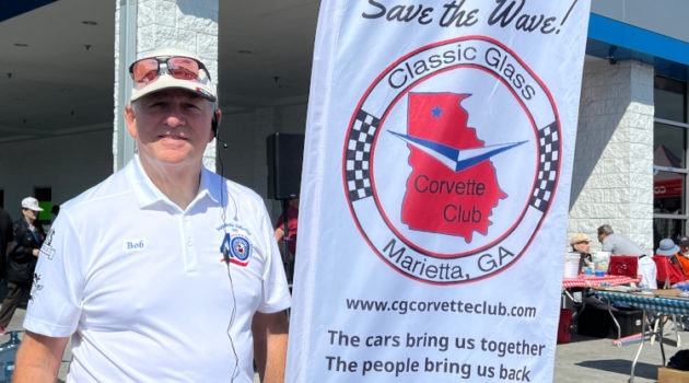 A man standing beside a Classic Glass Corvette club banner