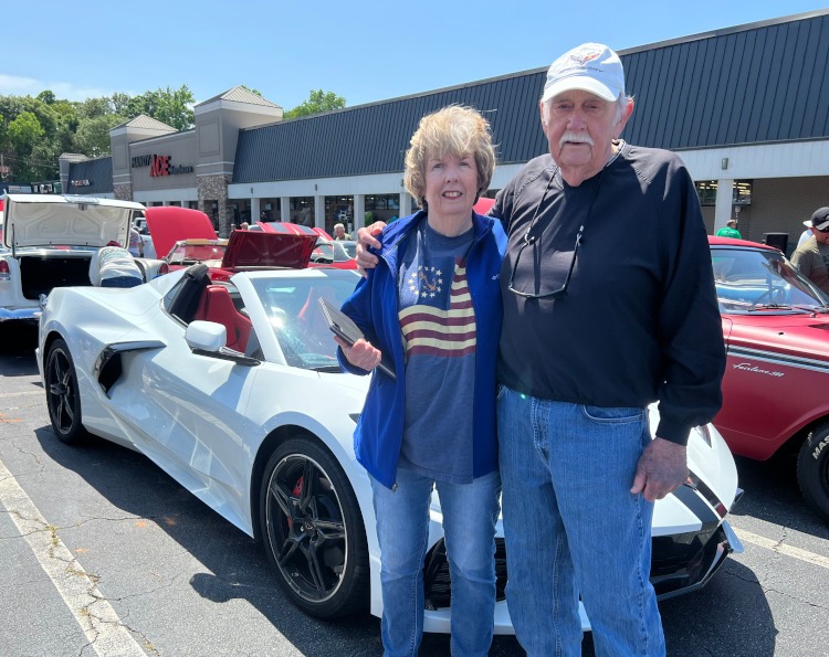 Two people are standing beside a C8 Corvette convertible.