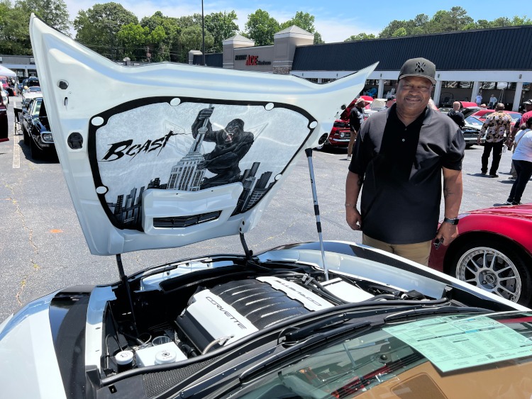 A man is posing beside the raised hood of a C7 Corvette.