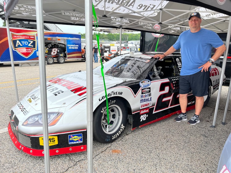 A man standing beside a classic NASCAR-type stock car.