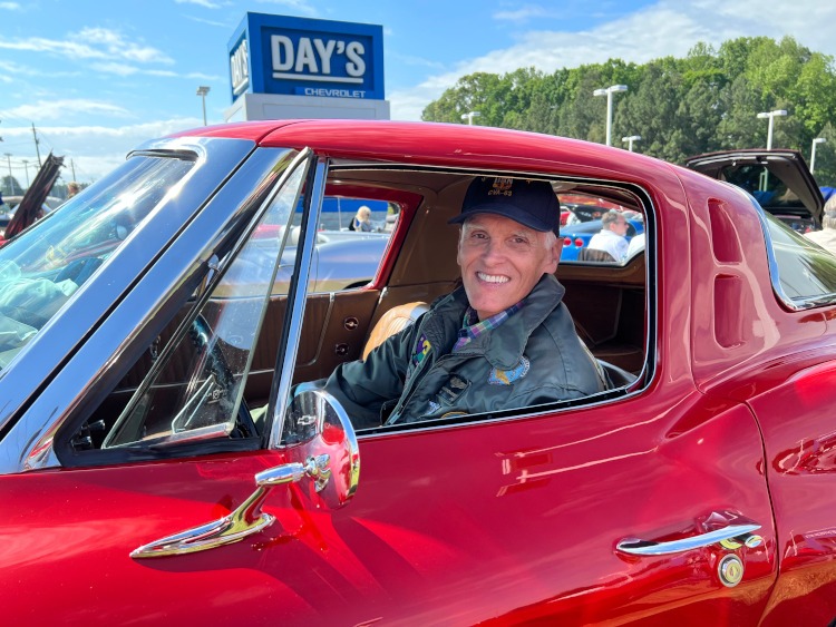 A Vietnam-era veteran is sitting in a red Corvette coupe.