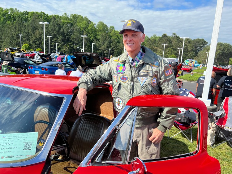 Vietnam-era veteran standing beside a red Corvette.