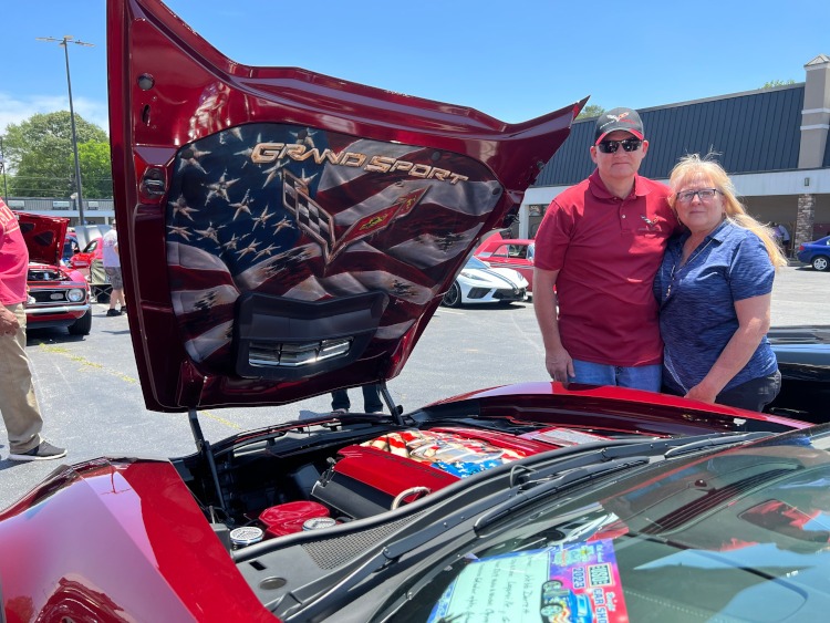 Two people are standing beside a Longbeach Red 2019 Corvette coupe.