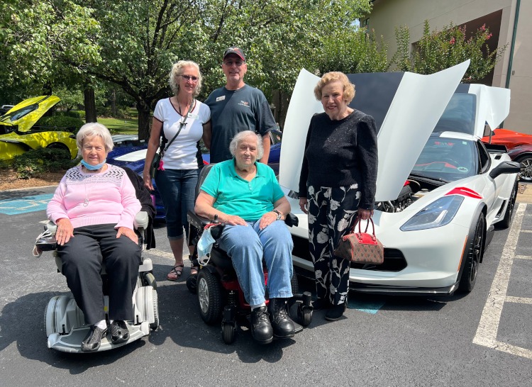 Five people are standing beside an Arctic White Grand Sport Corvette.