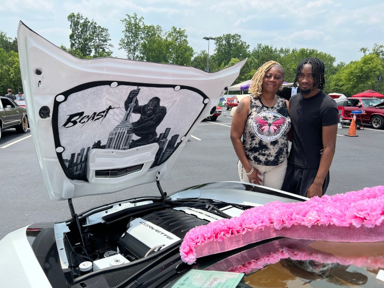 Two people are standing beside the raised hood of a Corvette.