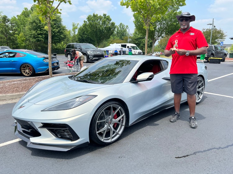 A man is standing beside a 2021 Silver Flair Corvette coupe.