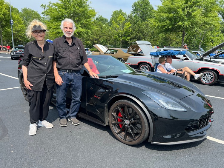 Two people are standing beside a 2017 Corvette convertible at a car show.
