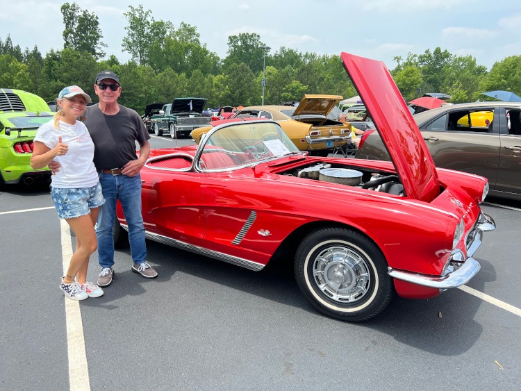Two people are posing beside a first-generation Corvette.