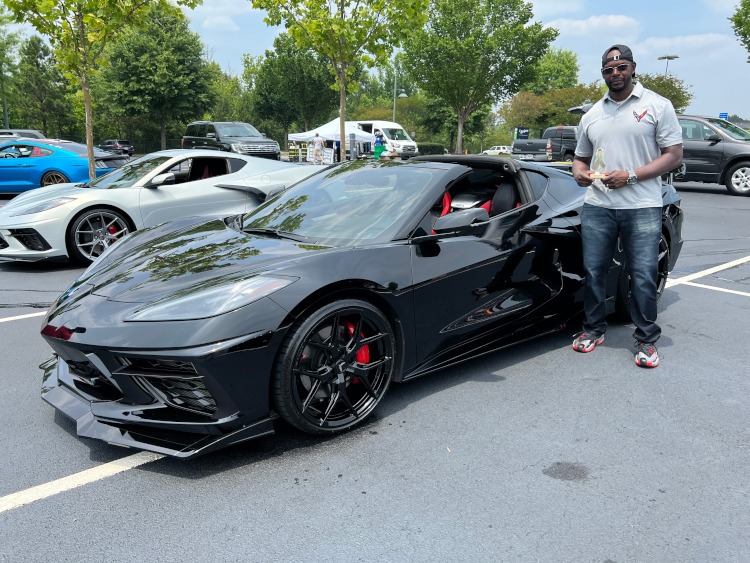 A man is standing beside a 2022 C8 black Corvette coupe.