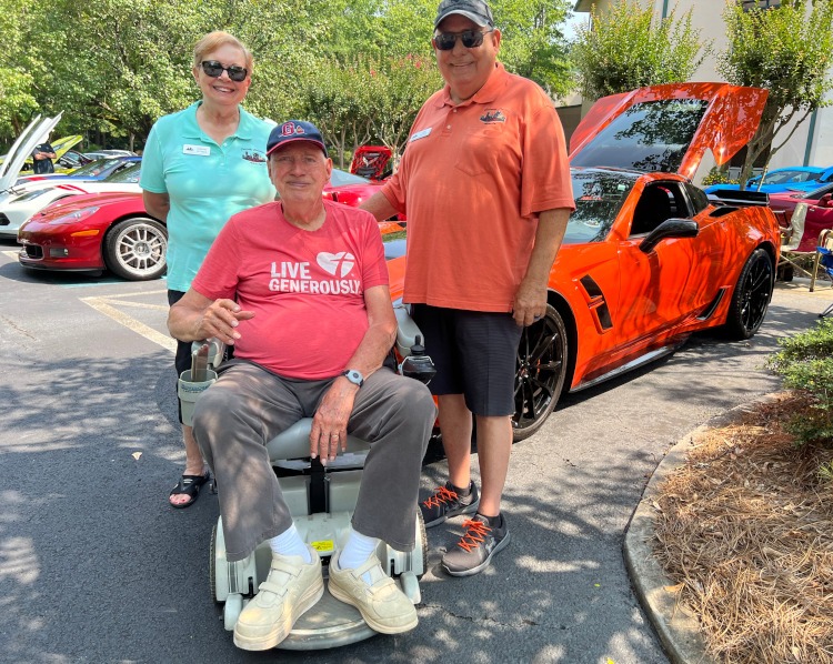 Three standing beside a C7 Sebring Orange Corvette coupe.