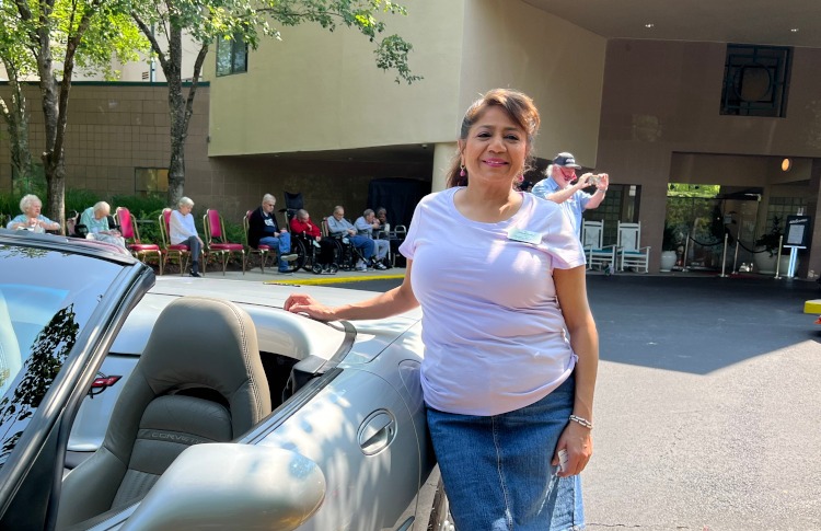 A woman was standing beside a 1998 silver Corvette convertible.
