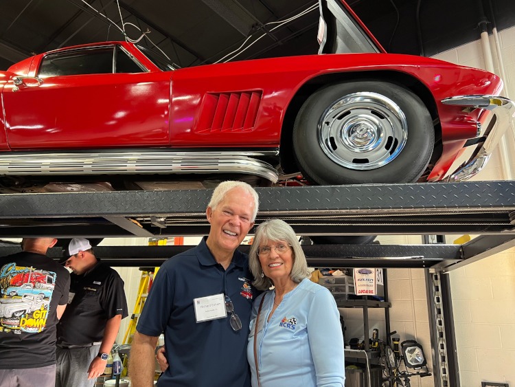 Two people are standing beside a red Corvette