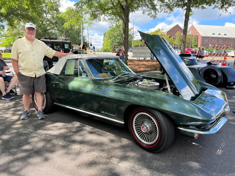 A man stands beside a 1967 green Corvette convertible.