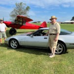 A Corvette and a red prop airplane at an aerodrome.