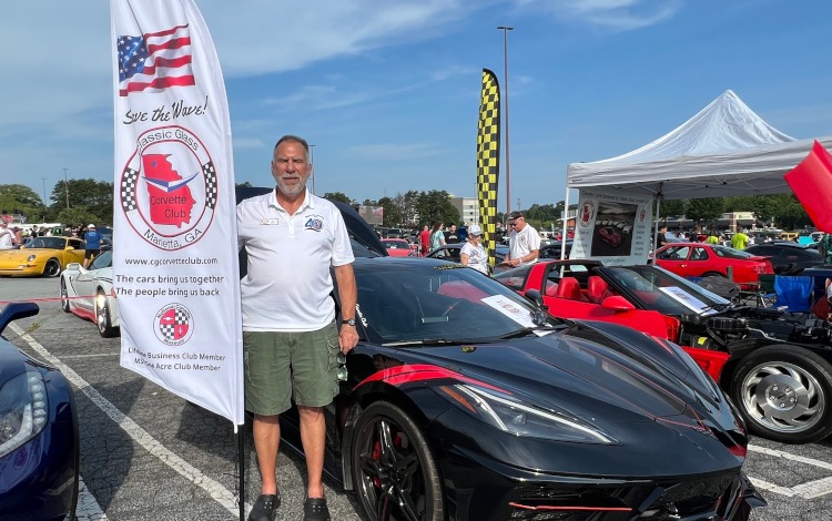 A man is standing beside a Corvette at a car show.