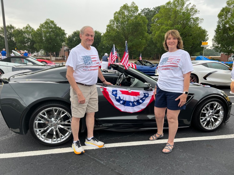 Two people are standing beside a Corvette Grand Sport coupe.