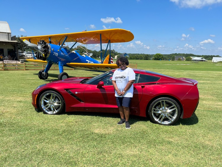 A woman is standing beside a C7 red Corvette coupe.