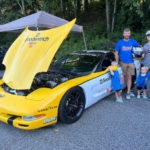 People standing beside a yellow 2001 Corvette.