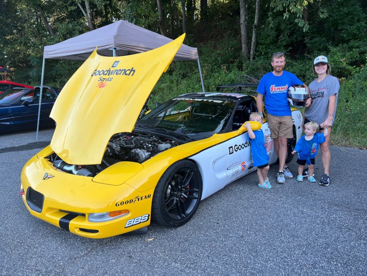 People standing beside a yellow 2001 Corvette.