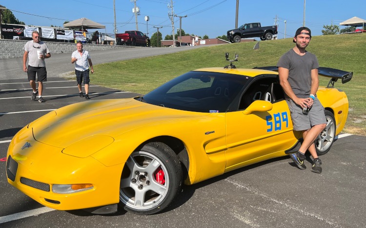 A man is leaning against a yellow 2003 Z06 Corvette.