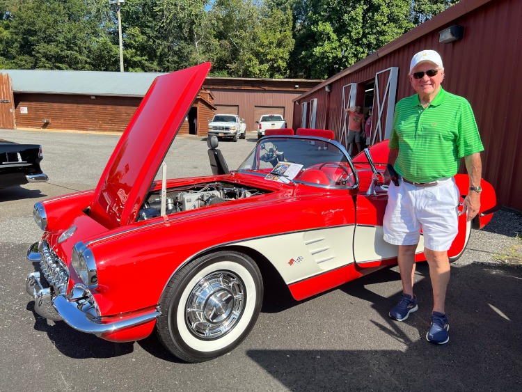 A man stands beside a 1960 red Corvette.