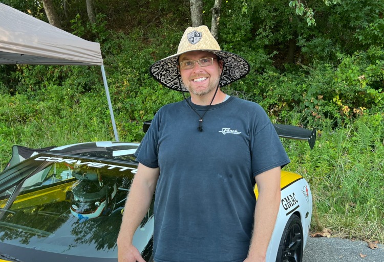 A man with a straw hat standing beside a car