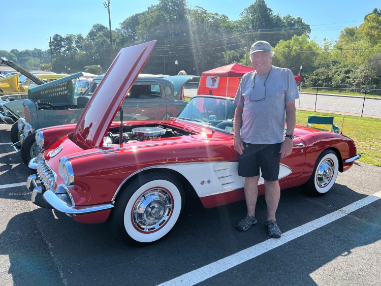A man stands beside a 1960 red Corvette roadster.