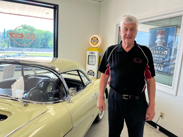 A man is standing indoors beside a classic Corvette.