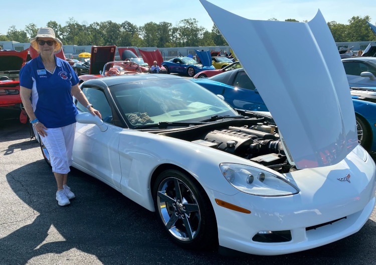 A woman standing beside a white Corvette.