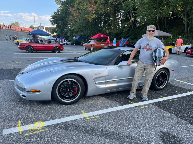 A man stands beside a silver Z06 Corvette coupe