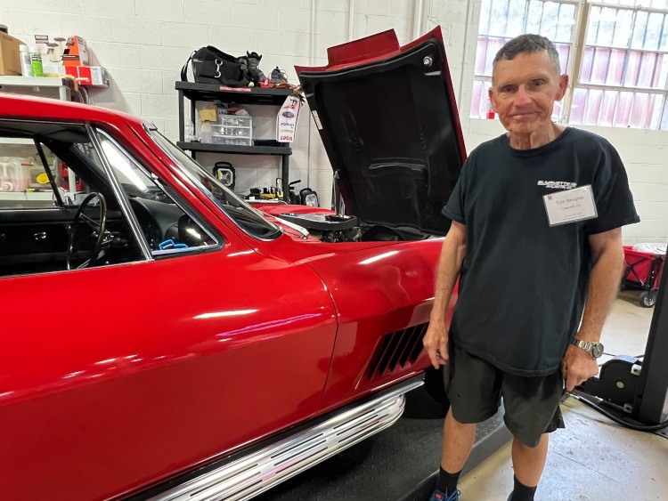 A man is standing beside a classic red Corvette.