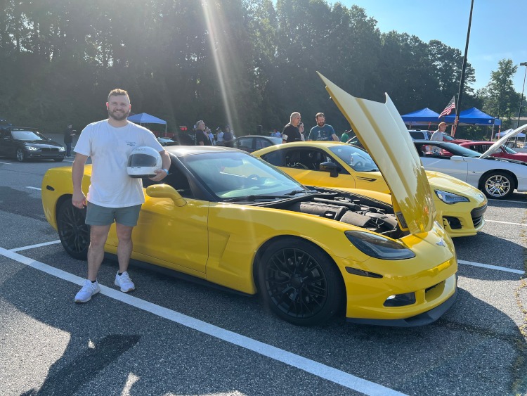 A man stands beside a C6 yellow Corvette