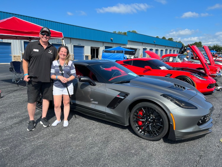 Two people are standing beside a supercharged Z06 Corvette.