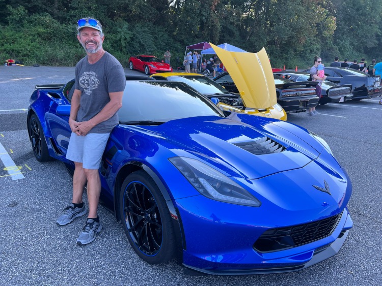 A man stands beside a seventh-generation blue Corvette coupe .
