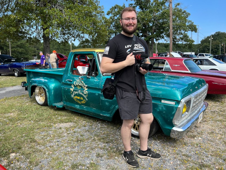 A man is holding a camera at a car show.