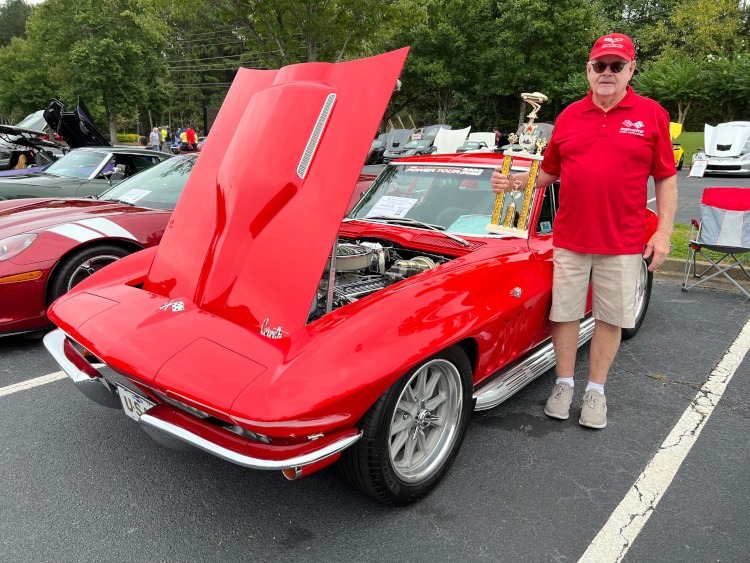 A man holding a trophy beside his red 1966 Corvette coupe