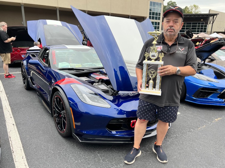A man holding a trophy beside a blue 2017 Corvette coupe.