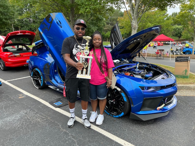 Two people are holding a trophy beside a 2016 blue Camaro SS