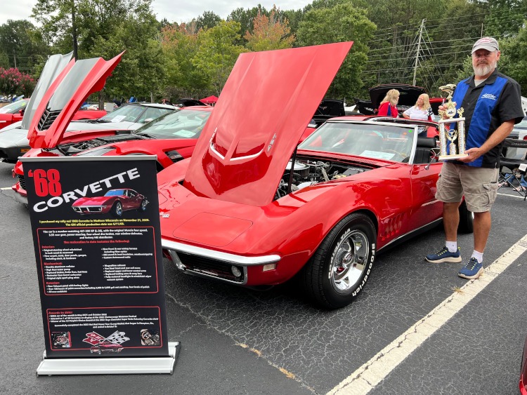 A man holding a trophy beside a 1968 Corvette coupe