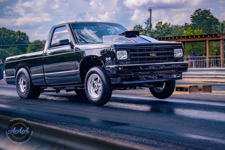 A pickup truck pulls the front wheels on a dragstrip.