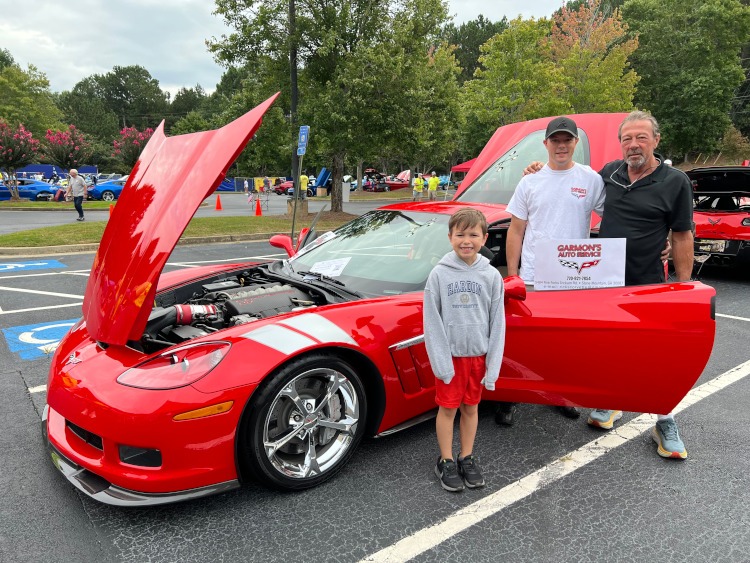 People standing beside a red sixth-generation Corvette Grand Sport.