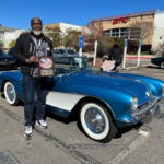 A man holding a trophy beside a blue 1957 Corvette