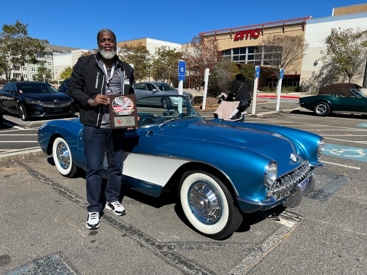 A man holding a trophy beside a blue 1957 Corvette
