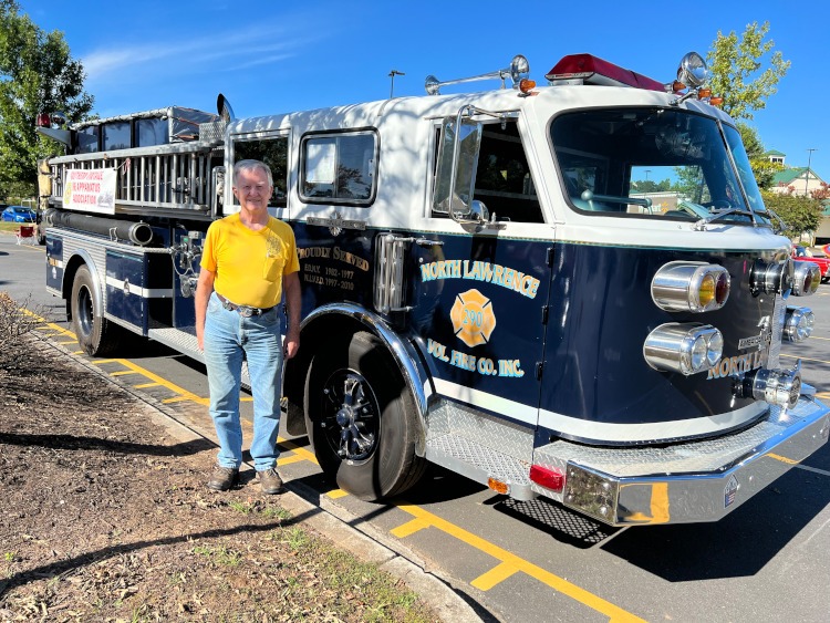 A man standing beside a blue fire truck at a car show.