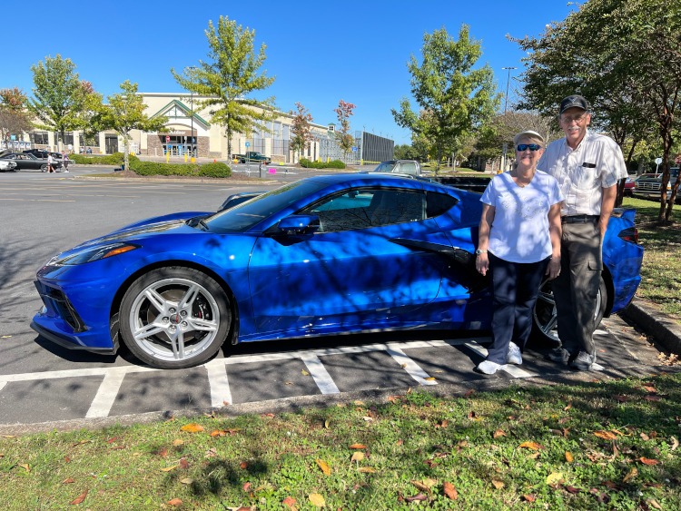 A couple standing beside a C8 Corvette coupe at a car show.