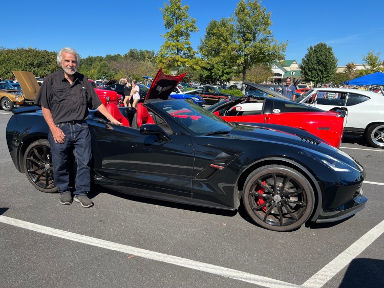 A man standing beside a C7 Corvette black convertible.