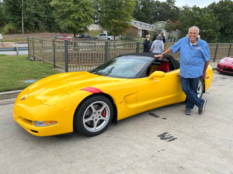 A man is standing beside a yellow Corvette convertible.