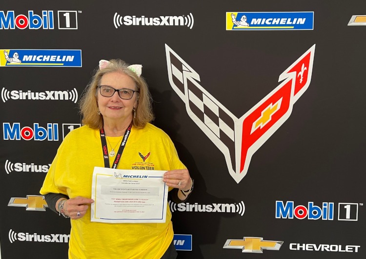 A woman holding a certificate beside a Corvette logo.