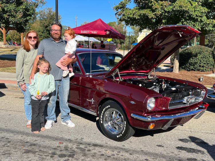 People standing around a burgandy classic Mustang.