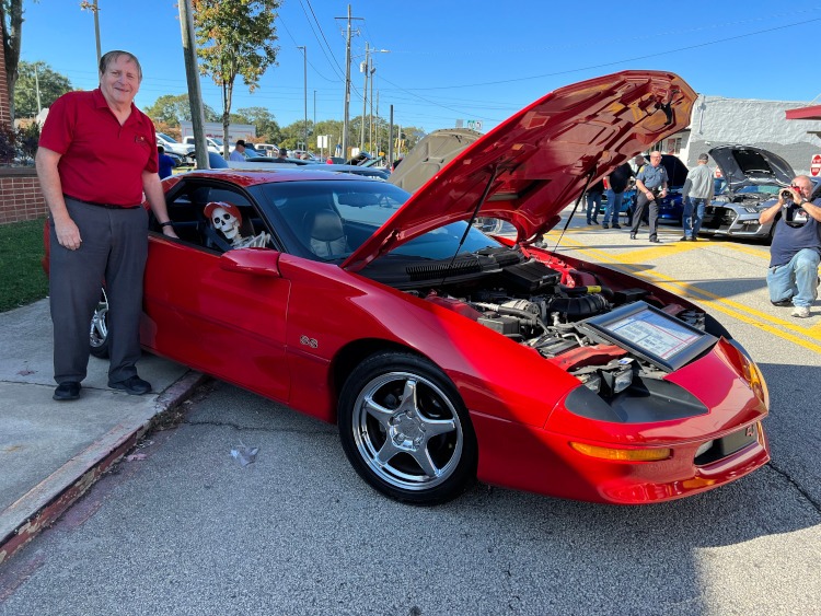 A man is standing beside his red Camaro coupe.